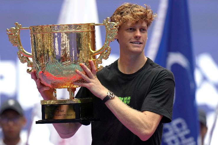 Jannik Sinner, tennista italiano, celebra la sua vittoria al torneo con un trofeo alzato in mano, sorridendo felice nel 2025.