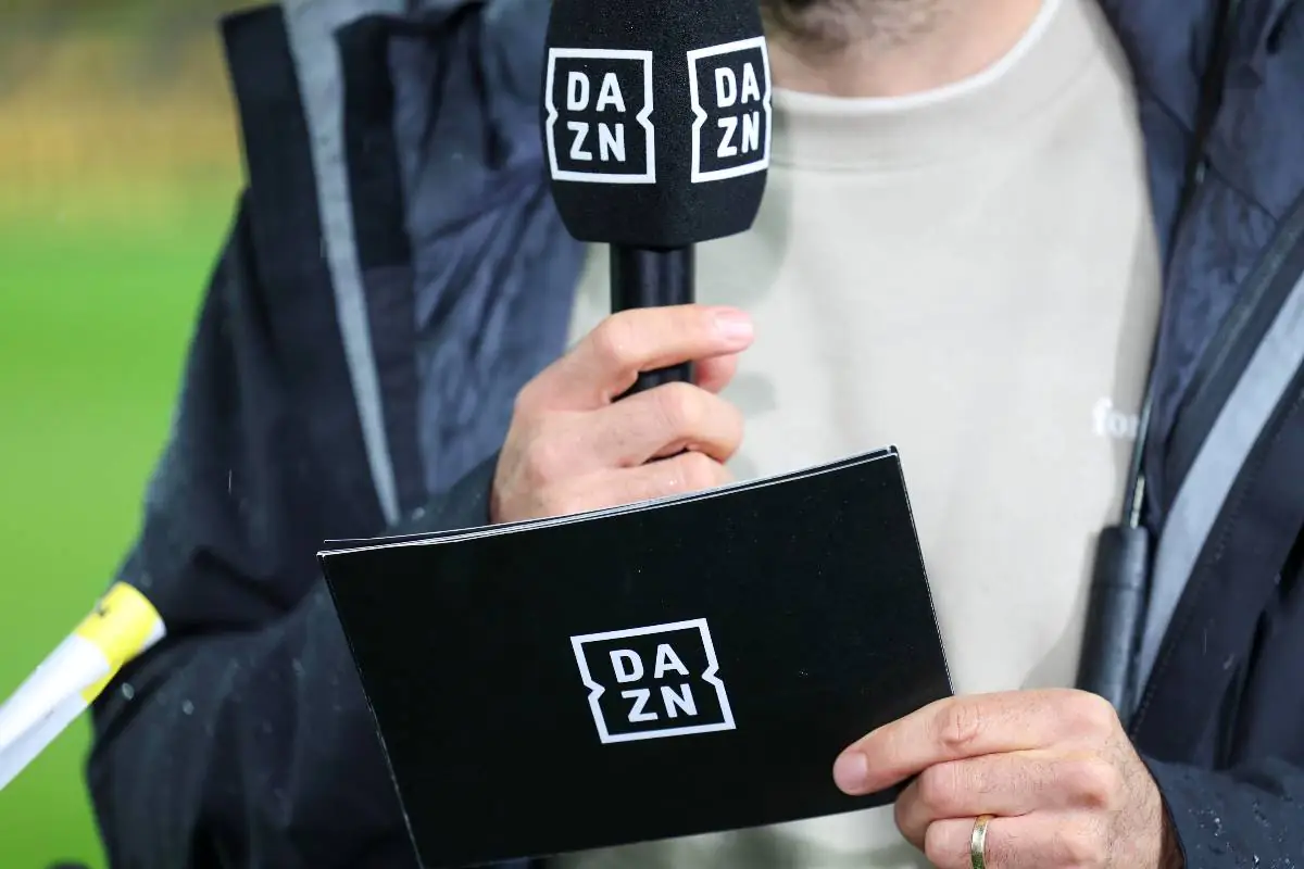 Giornalista DAZN tiene microfono e taccuino durante una diretta di Serie A 2025 allo stadio.