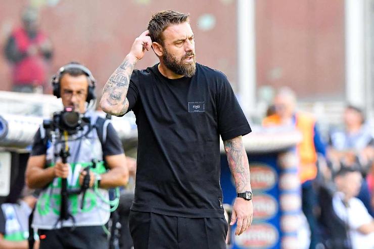 Daniele De Rossi a bordo campo durante una partita della Roma, con espressione concentrata e atteggiamento riflessivo.