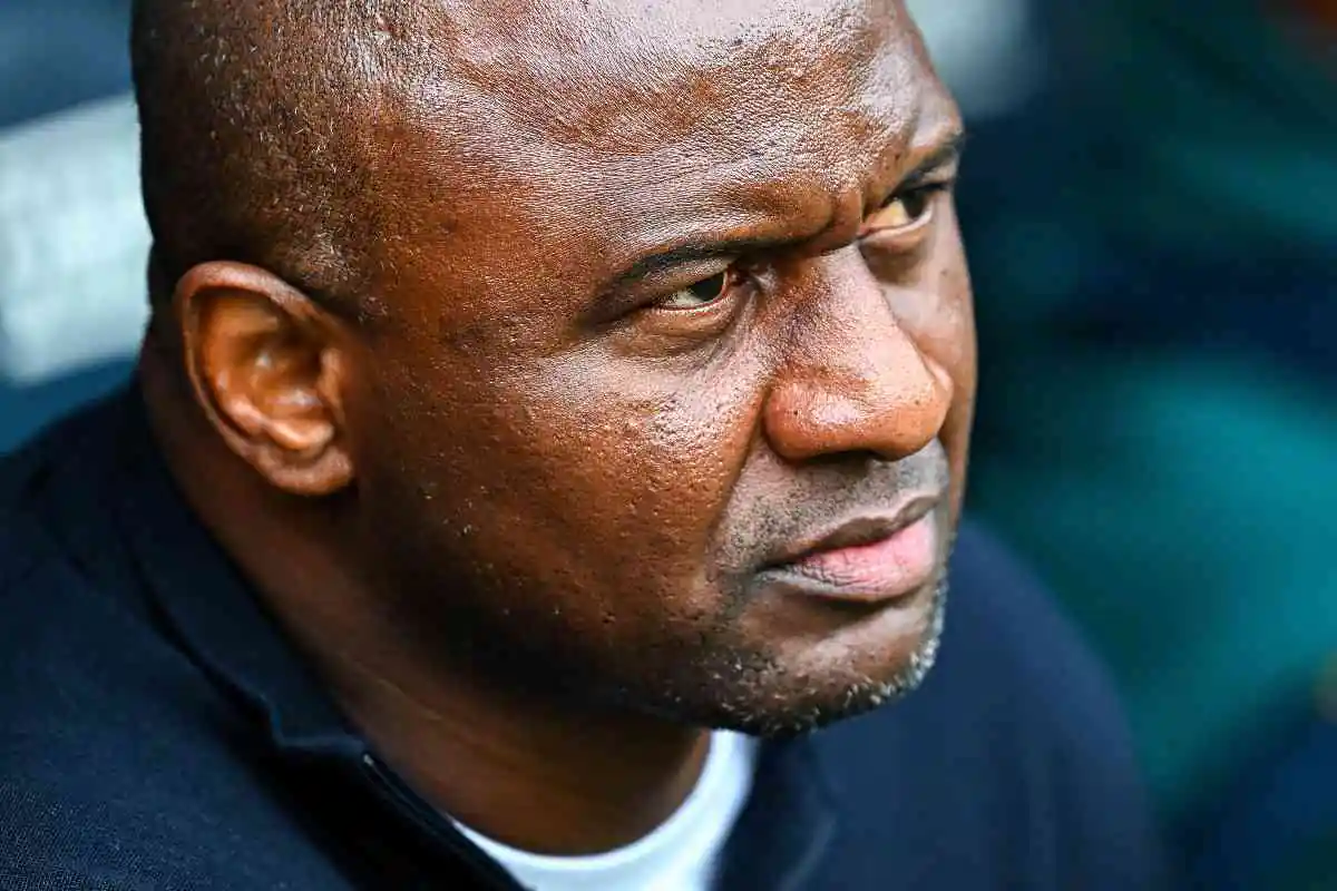 Patrick Vieira osserva concentrato dalla panchina durante una partita della stagione 2025, espressione intensa e sguardo fisso sul campo.
